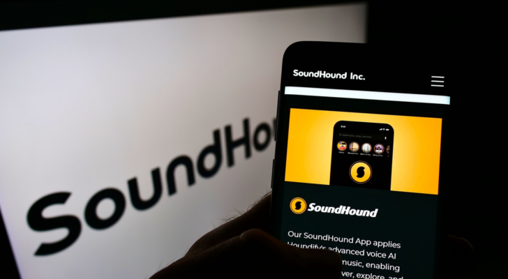 Person holding smartphone with webpage of US audio recognition company SoundHound Inc. (SOUN) on screen in front of logo. Focus on center of phone display. Unmodified photo.