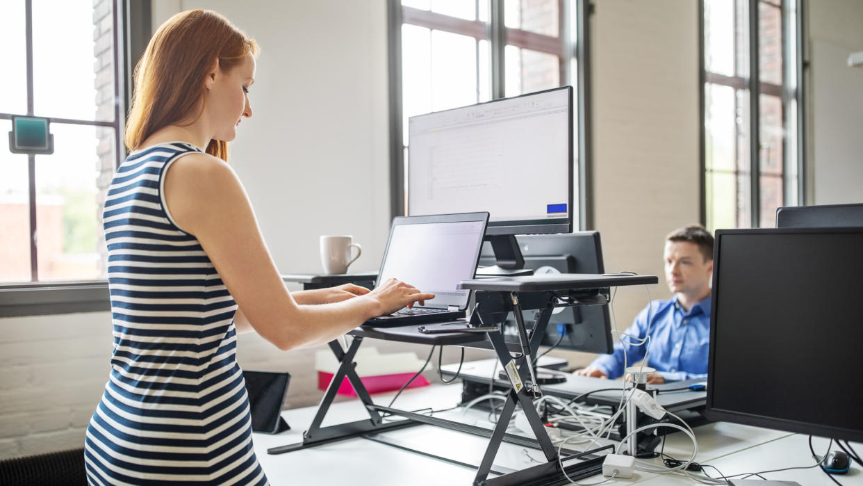 Business woman working on laptop computer at ergonomic standing desk.