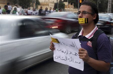 A demonstrator looks on with a sign reading "I am against the military courts for civilians" taped over his mouth during a human chain by members of the April 6 movement and liberal activists against a law restricting demonstrations as well as the crackdown on activists and calling for the release of activists in detention in front of El-Thadiya Egyptian Presidential in Cairo, April 23, 2014. The sign reads "Freedom for Abdallah Elshamy, an Egyptian journalist for Al Jazeera Arabic broadcast." REUTERS/Amr Abdallah Dalsh