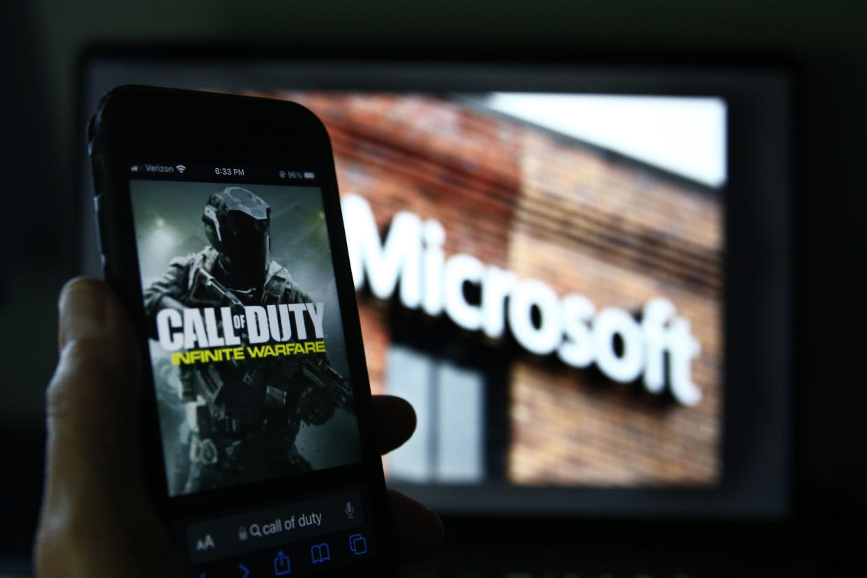 An image from Activision's Call of Duty is shown on a smartphone near a photograph of the Microsoft logo.