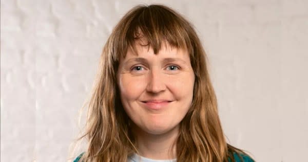 The photograph is a headshot of Lisa Connell, co-founder of Mother queer space. In the image she is looking directly into the camera smiling with her mouth closed. She has long sandy coloured hair worn loose with a fringe.