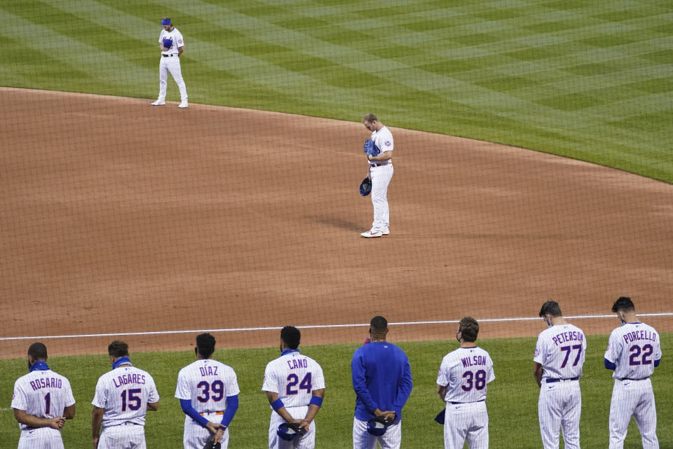 The New York Mets and the Miami Marlins stand on the field and bow their heads at the start of their baseball game before walking off in protest, Thursday, Aug. 27, 2020, in New York. The teams jointly walked off the field after a moment of silence, draping a Black Lives Matter T-shirt across home plate as they chose not to start their scheduled game Thursday night. (AP Photo/John Minchillo)