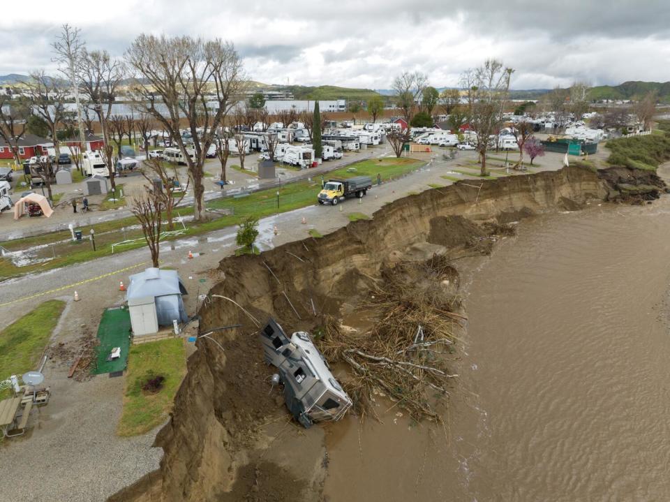 A recreational vehicle lies at the bottom of a cliff by a river.