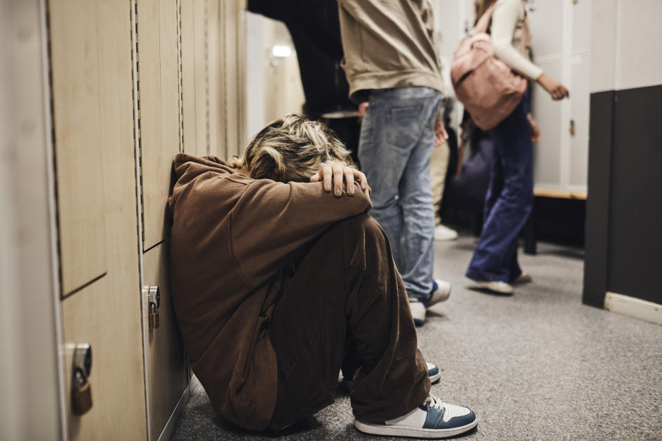 A kid hunches over and covers his face as he sits in the school hallway