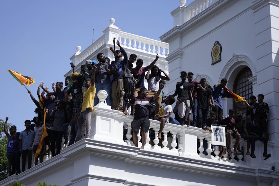 Sri Lankan protesters, some holding national flags, after storming the Prime Minister Ranil Wickremesinghe's office, demanding he resign after president Gotabaya Rajapaksa fled the country amid economic crisis in Colombo, Sri Lanka, Wednesday, July 13, 2022. Rajapaksa fled on a military jet on Wednesday after angry protesters seized his home and office, and appointed Prime Minister Ranil Wickremesinghe as acting president while he is overseas. Wickremesinghe quickly declared a nationwide state of emergency to counter swelling protests over the country's economic and political collapse. (AP Photo/Eranga Jayawardena)