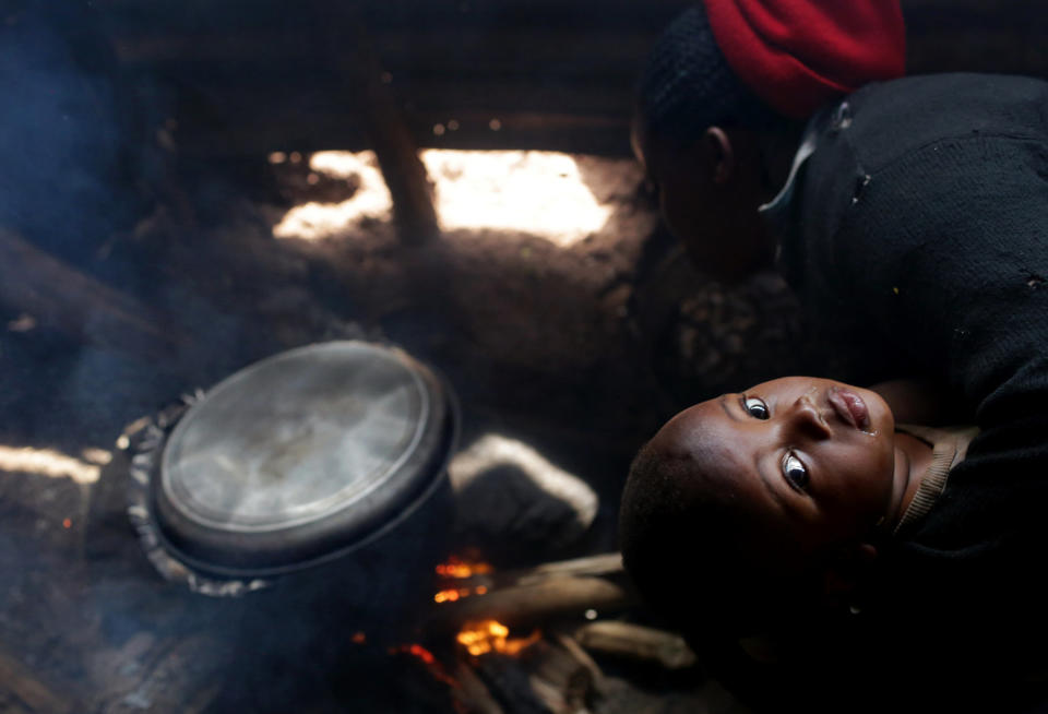 Marie Claire Nyirahabumufasha, 31-year-old mother to Nayituriki Bienvenu, holds her one-year-old as she cooks potatoes in a small hut near her restaurant in Kigali village in Rwanda, on November 12, 2017. Marie Claire hires others to bring her wood for cooking, and says her eyes and throat often hurt from doing so over smoke. She added she would definitely prefer using biogas over firewood if she had the option. (Photograph by Yana Paskova)  