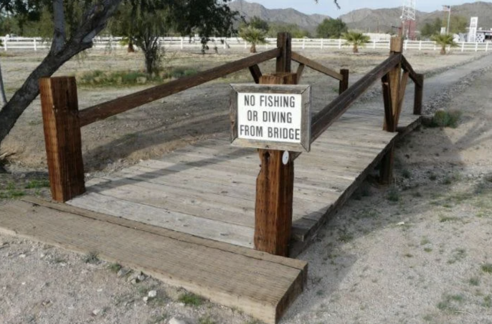 Wooden bridge in a dry area with a sign that reads 'NO FISHING OR DIVING FROM BRIDGE.'