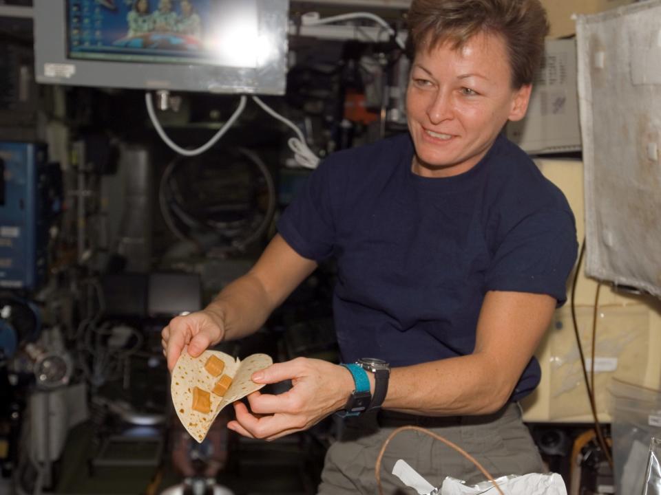 Astronaut Peggy Whitson holds up a tortilla with cheese cubes on the space station