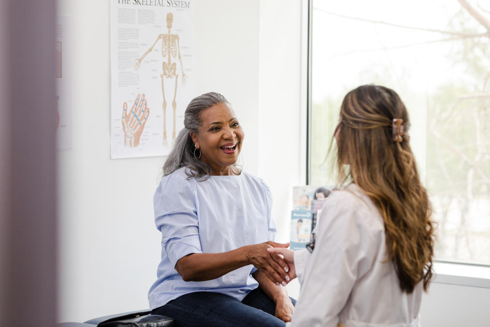 The mature woman smiles while shaking hands with the female healthcare professional as she introduces herself.