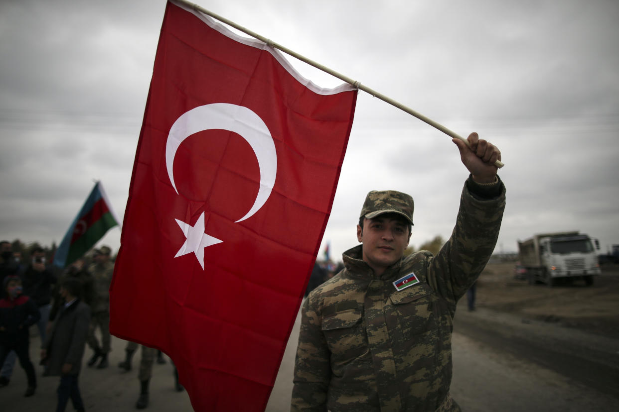 An Azerbaijani soldier holds a Turkish national flag as he celebrates the transfer of the Lachin region to Azerbaijan's control, as part of a peace deal that required Armenian forces to cede the Azerbaijani territories they held outside Nagorno-Karabakh, in Aghjabadi, Azerbaijan, Tuesday, Dec. 1, 2020. Azerbaijan has completed the return of territory ceded by Armenia under a Russia-brokered peace deal that ended six weeks of fierce fighting over Nagorno-Karabakh. Azerbaijani President Ilham Aliyev hailed the restoration of control over the Lachin region and other territories as a historic achievement. (AP Photo/Emrah Gurel)