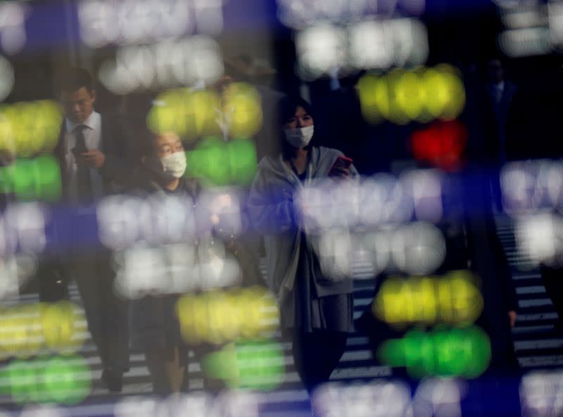 FILE PHOTO: Pedestrians wearing facial masks are reflected on an electric board showing stock prices outside a brokerage at a business district in Tokyo