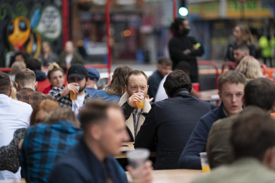 Members of the public are seen at a bar in Manchester's Northern Quarter, England, Saturday July 4, 2020. England is embarking on perhaps its biggest lockdown easing yet as pubs and restaurants have the right to reopen for the first time in more than three months. In addition to the reopening of much of the hospitality sector, couples can tie the knot once again, while many of those who have had enough of their lockdown hair can finally get a trim. (AP Photo/Jon Super)