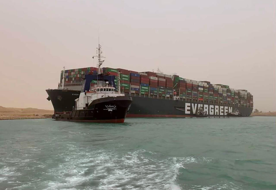 CORRECTS NAME OF SHIP TO EVER GIVEN, NOT EVER GREEN - In this photo released by the Suez Canal Authority, a boat navigates in front of a cargo ship, Ever Given, Wednesday, March 24, 2021, after it become wedged across Egypt’s Suez Canal and blocked all traffic in the vital waterway. An Egyptian official warned Wednesday it could take at least two days to clear the ship. (Suez Canal Authority via AP)