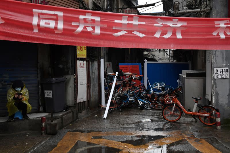 Volunteer keeps watch near an entrance blocked by barricades and shared bicycles at a residential area in Wuhan