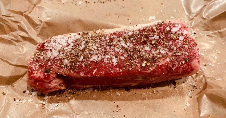 raw steak covered in pepper on brown paper