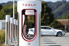 A white Tesla parked at a Tesla fast charging point.