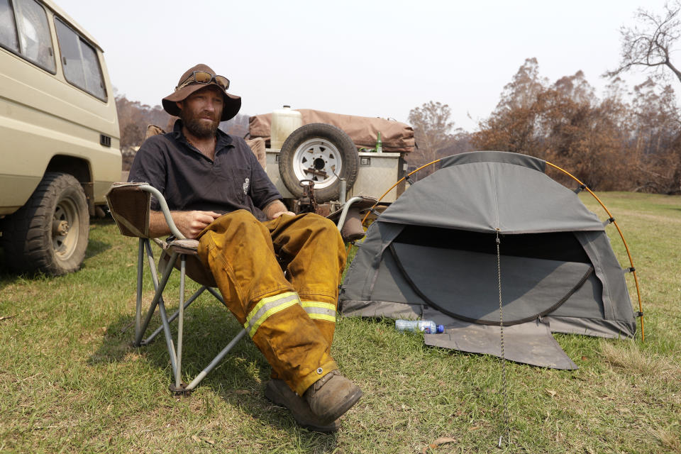 El bombero voluntario Ash Graham sentado el 13 de enero del 2020 junto a la carpa que instaló en la la estación de bomberos de Nerrigundah, Australia, donde está desde que un incendio forestal devastó el pueblo el 31 de diciembre del 2019. (AP Photo/Rick Rycroft)