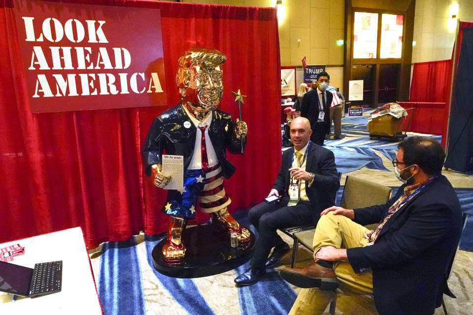 Look Ahead America sponsor Matt Braynard, center, talks to conference attendees at his booth in the merchandise show with a statue of former president Donald Trump at the Conservative Political Action Conference (CPAC) Friday, Feb. 26, 2021, in Orlando, Fla. (AP Photo/John Raoux)