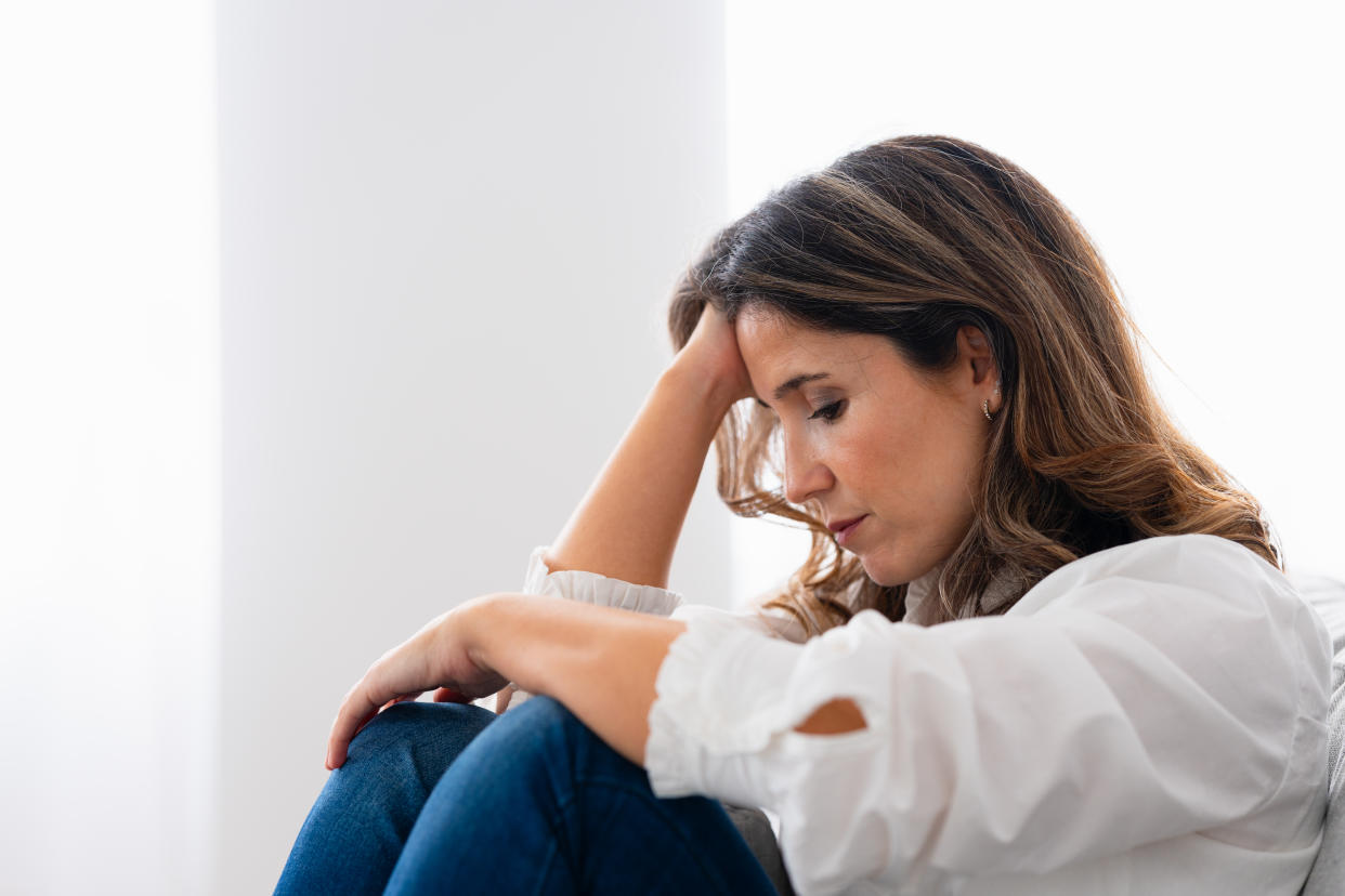 Side view of a woman sitting at home with a sad look on her face.