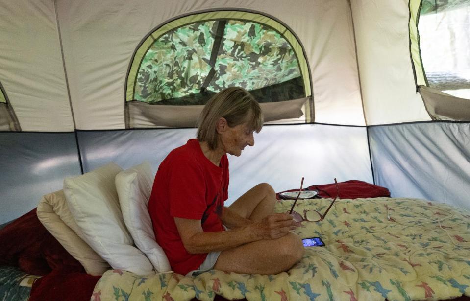 Mary Ellen Mullen looks online with her phone as she enjoys a quiet morning in her tent. A homeless camp in the woods in Toms River on August 11, 2023