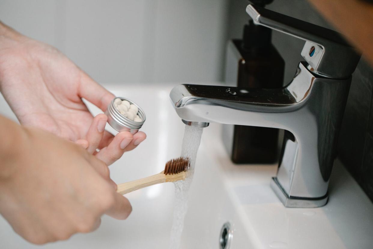 hands holding a toothbrush and toothpaste tablets in sink with running water