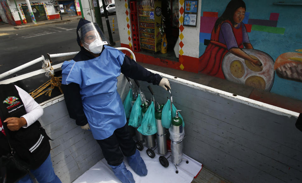 City worker Alexis Hernandez rides in the back of a cargo truck transporting tanks of oxygen for COVID-19 patients, in the Iztapalapa borough of Mexico City, Friday, Jan. 15, 2021. The city offers free oxygen refills for COVID-19 patients. (AP Photo/Marco Ugarte)
