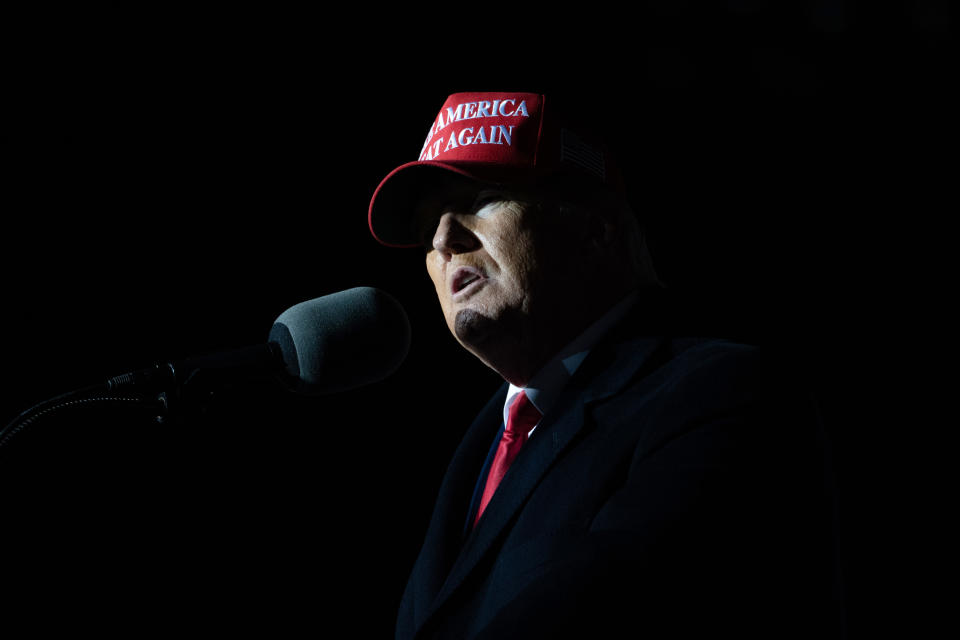 Former President Donald Trump, wearing a Make America Great Again hat, speaks into a microphone at a rally.