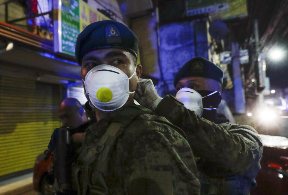 A Filipino army trooper helps his comrade wear a protective masks as they arrive to augment police at Valenzuela, metropolitan Manila, Philippines early Sunday March 15, 2020. Thousands of Philippine police, backed by the army and coast guard, have started sealing the densely populated capital from most domestic travelers in one of Southeast Asia's most drastic containment moves against the coronavirus. For most people, the new coronavirus causes only mild or moderate symptoms. For some, it can cause more severe illness, especially in older adults and people with existing health problems. (AP Photo/Aaron Favila)