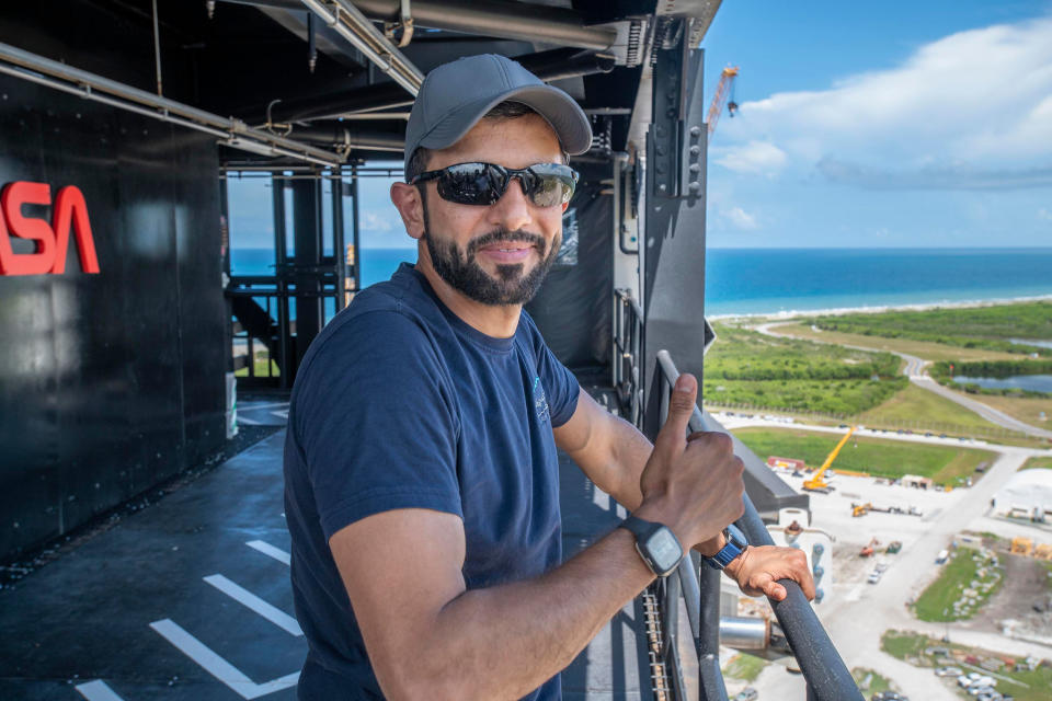 person giving a thumbs-up in a tower above a launch pad area, with ocean in the background