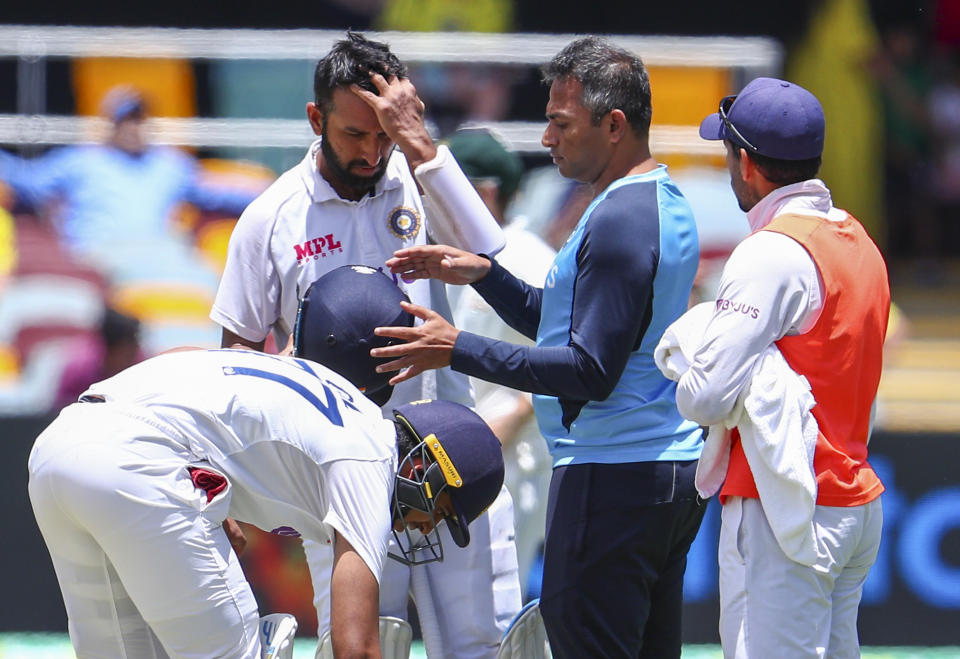 India's Cheteshwar Pujara is checked by a trainer after he was hit on the helmet while batting during play on the final day of the fourth cricket test between India and Australia at the Gabba, Brisbane, Australia, Tuesday, Jan. 19, 2021. (AP Photo/Tertius Pickard)