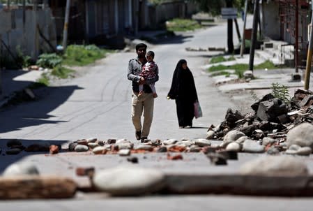 A Kashmiri familiy walks past a blockade put up by residents to prevent Indian security force personnel from entering their neighborhood during restrictions, in Srinagar