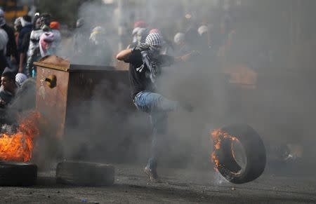 A Palestinian protester kicks a burning tyre during clashes with Israeli troops near the Jewish settlement of Bet El, near the West Bank city of Ramallah, October 29, 2015. REUTERS/Mohamad Torokman