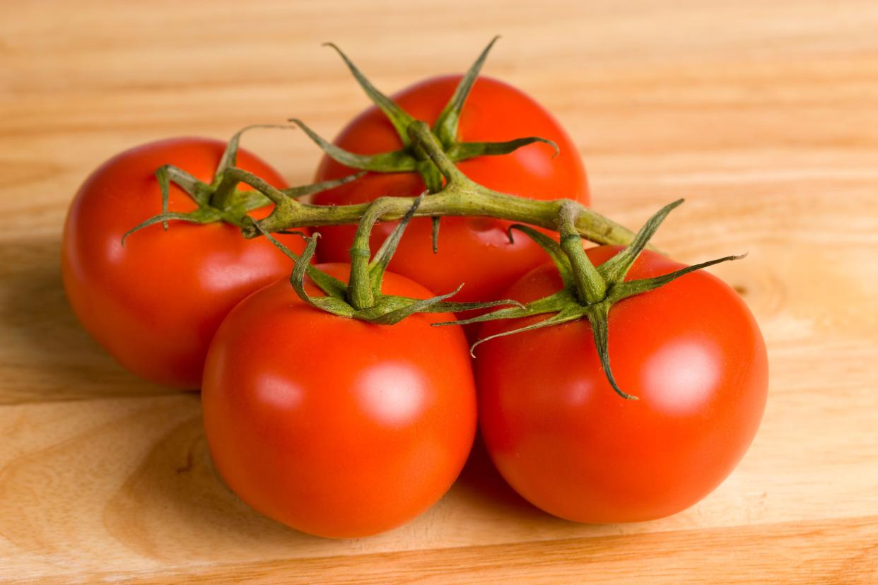 Four ripe tomatoes on a vine on a wooden kitchen table