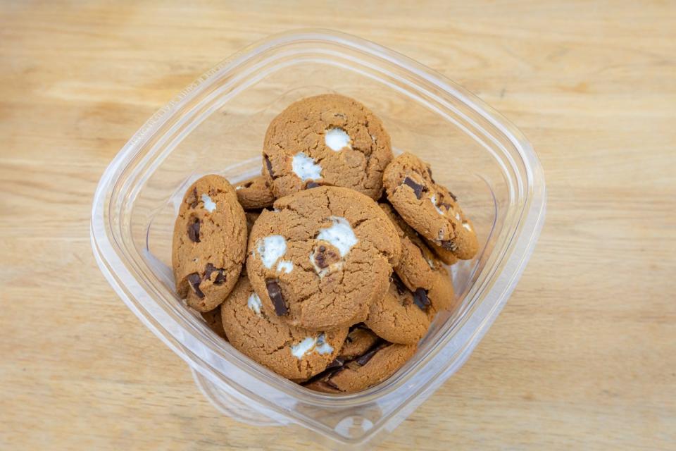 Gold cookies with marshmallows and chocolate chunks in a plastic container on a counter 