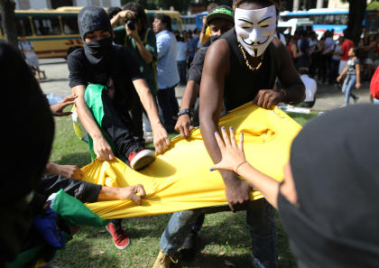 Masked anti-World Cup protesters rip apart a Brazilian national team soccer jersey on Thursday. (AP)