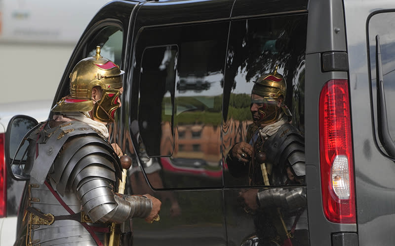 A man wearing a Roman Centurion costume uses the windshield of a car as a mirror