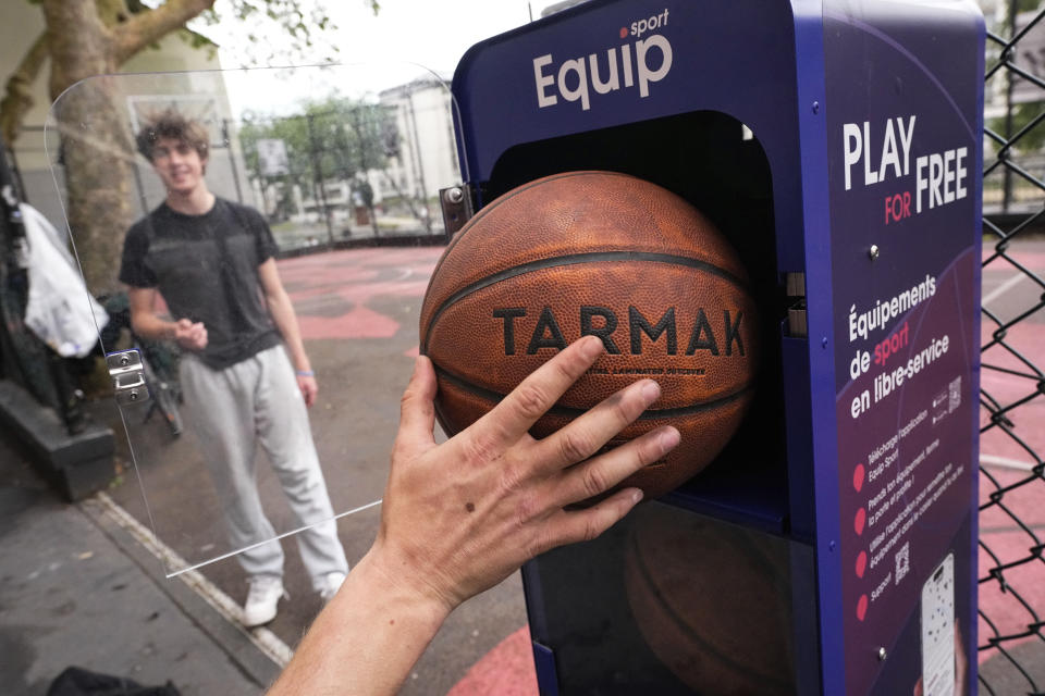 A man puts back a basketball into a free self-service sports equipment station next to a basketball court along the canal Saint Martin in Paris Sunday, June 16, 2024. New names will soon adorn replica NBA jerseys of French youths competing on basketball courts around Paris. Frenchmen Zaccharie Risacher, Alexandre Sarr and Tidjane Salaün are among the top picks in the NBA draft, where a second straight French No. 1 pick is expected after Victor Wembanyama last year. (AP Photo/Michel Euler)