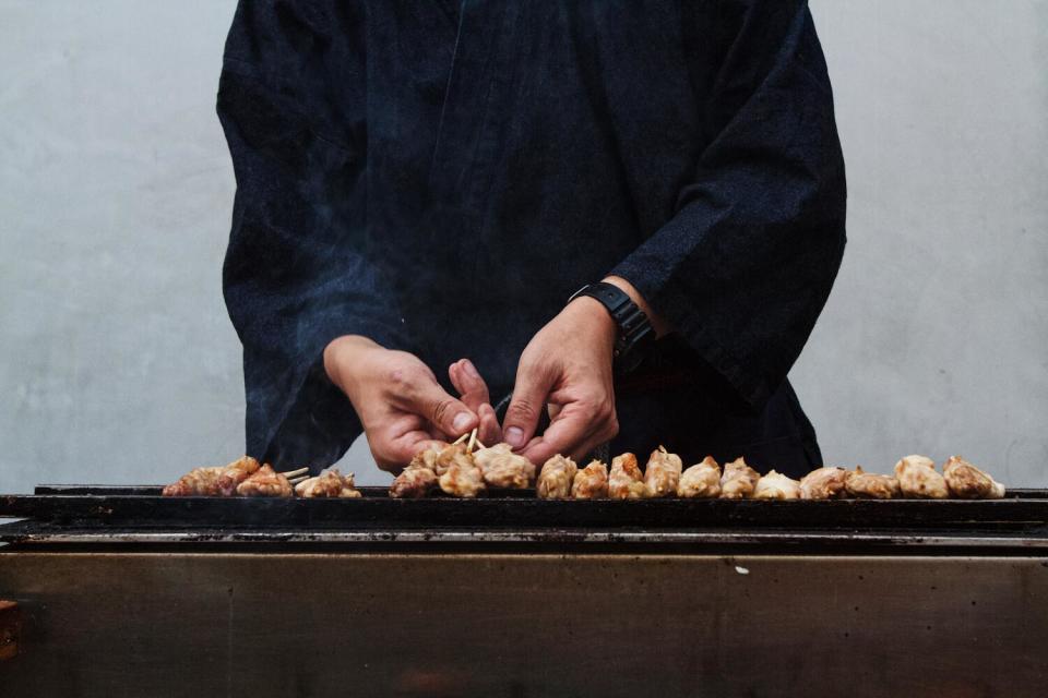 A closeup of hands holding a cluster of chicken skewers