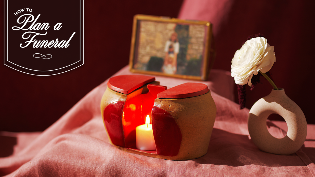 beige and red double urn with candle in the middle surrounded by flower and picture frame