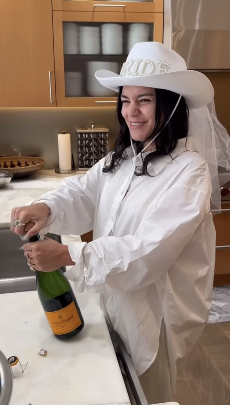 Close-up of Vanessa wearing a Western-style hat and opening a bottle of champagne in a kitchen