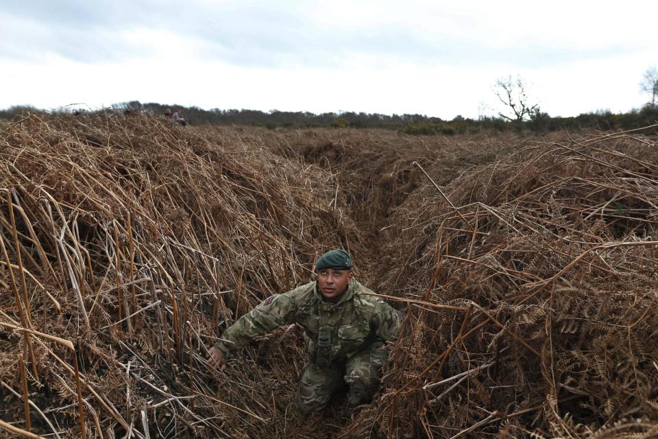 British army Lance Corporal Rob Walters kneels on a WW1 practise trench as he poses for the photographers in Gosport, southern England, Thursday, March 6, 2014. This overgrown and oddly corrugated patch of heathland on England’s south coast was once a practice battlefield, complete with trenches, weapons and barbed wire. Thousands of troops trained here to take on the Germany army. After the 1918 victory _ which cost 1 million Britons their lives _ the site was forgotten, until it was recently rediscovered by a local official with an interest in military history. Now the trenches are being used to reveal how the Great War transformed Britain _ physically as well as socially. As living memories of the conflict fade, historians hope these physical traces can help preserve the story of the war for future generations. (AP Photo/Lefteris Pitarakis)
