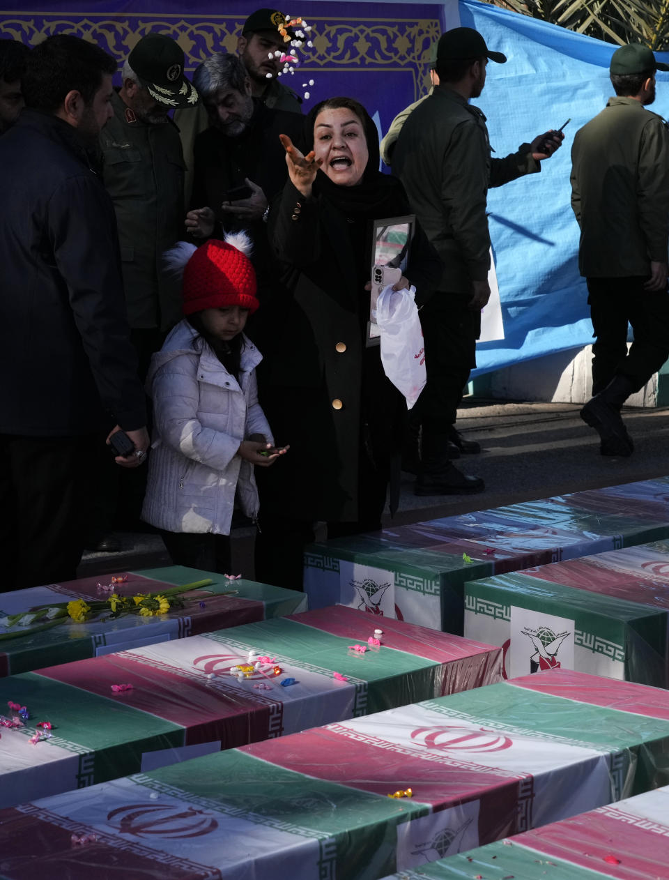A woman throws candy over the flag-draped coffin of her son who was killed in Wednesday's bomb explosion, during the victims funeral ceremony in the city of Kerman about 510 miles (820 kms) southeast of the capital Tehran, Iran, Friday, Jan. 5, 2024. Iran on Friday mourned those slain in an Islamic State group-claimed suicide bombing targeting a commemoration for a general slain in a U.S. drone strike in 2020. (AP Photo/Vahid Salemi)