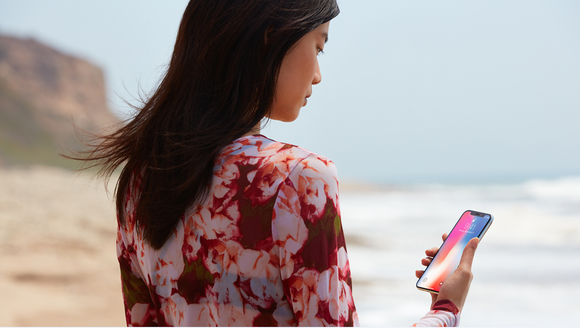 A woman holding an Apple iPhone X on the beach.