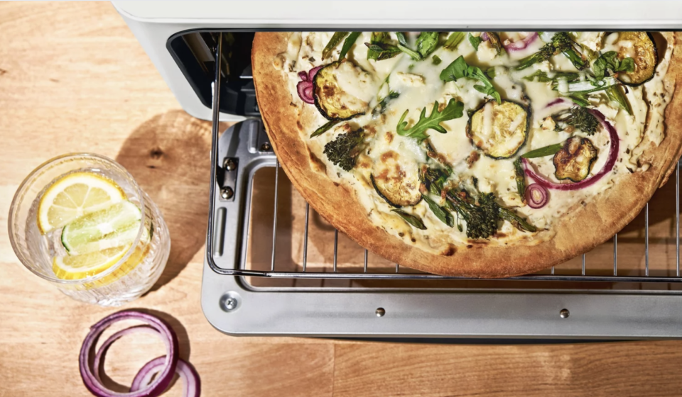 The Drew Barrymore Beautiful Infrared Air Fry Toaster Oven is shown cooking a pizza.