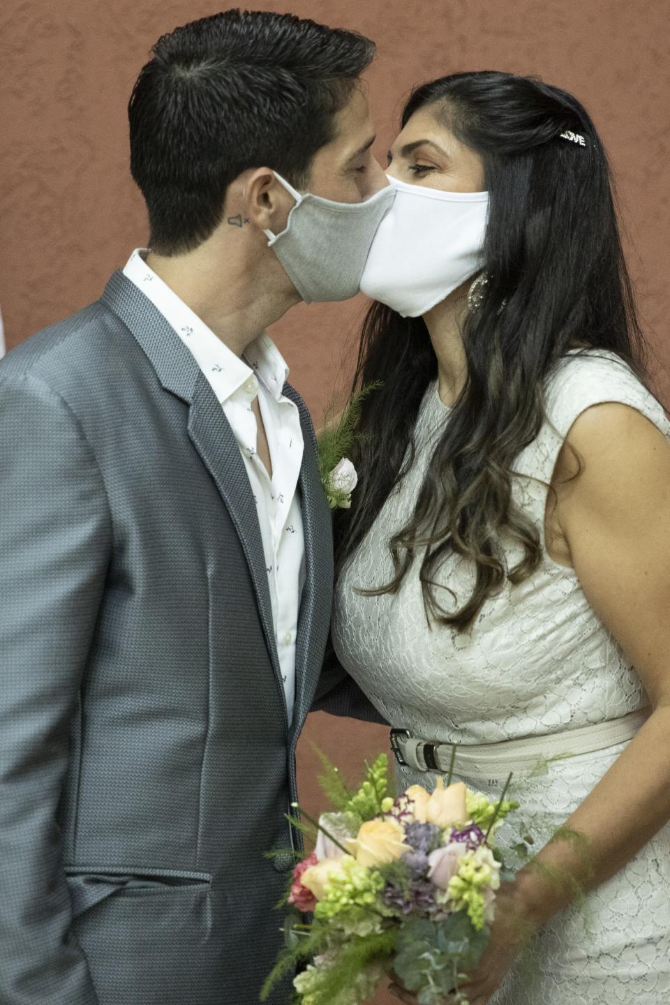 Groom Manuel Soria and bride Loris Sanchez, wearing protective face masks as a precaution against the spread of the new coronavirus, share a kiss during their wedding ceremony at the Civil Registry office, in Asuncion, Paraguay, Saturday, June 13, 2020. (AP Photo/Jorge Saenz)