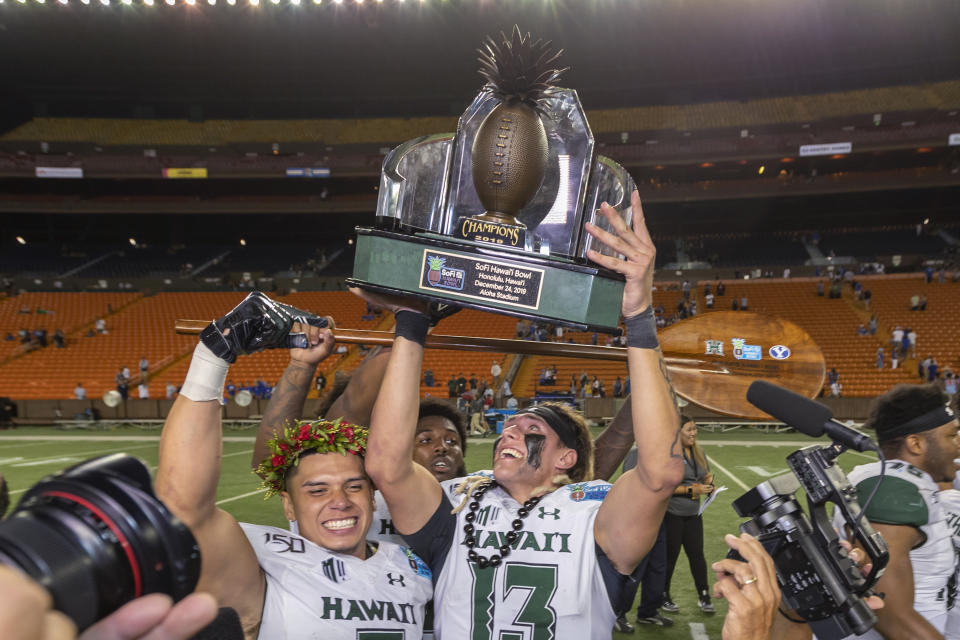 Hawaii quarterback Cole McDonald (13) holds up the Hawaii Bowl trophy, next to wide receiver Jason-Matthew Sharsh, left, after the team's 38-34 win over BYU in the NCAA college football game Tuesday, Dec. 24, 2019, in Honolulu. (AP Photo/Eugene Tanner)