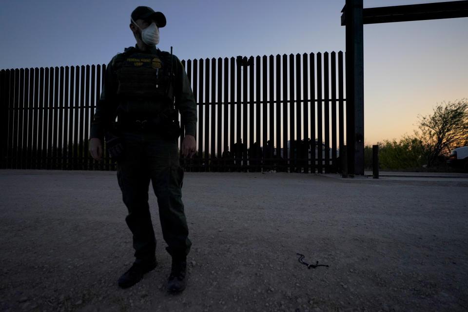 A U.S. Customs and Border Protection agent looks on near a gate on the U.S.-Mexico border wall as agents take migrants into custody, Sunday, March 21, 2021, in Abram-Perezville, Texas. The fate of thousands of migrant families who have recently arrived at the Mexico border is being decided by a mysterious new system under President Joe Biden. U.S. authorities are releasing migrants with “acute vulnerabilities” and allowing them to pursue asylum. But it’s not clear why some are considered vulnerable and not others. (AP Photo/Julio Cortez)