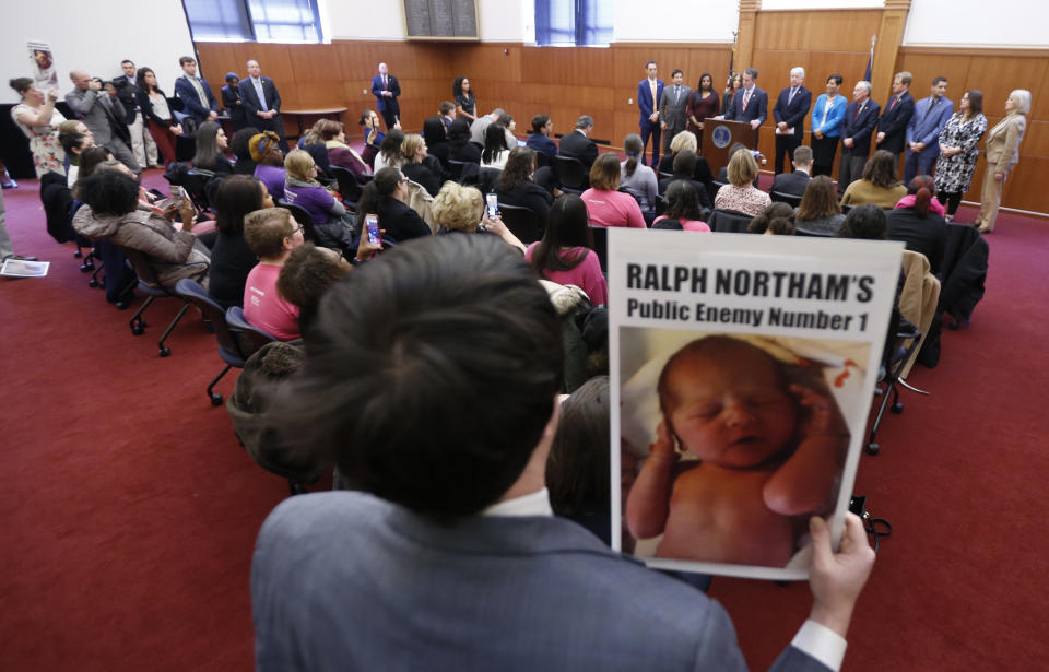 A demonstrator holds a sign as Gov. Ralph Northam, at podium, gives a news conference at the Capitol in Richmond, Va., Thursday, Jan. 31, 2019. Northam made a statement and answered questions about the late term abortion bill that was killed in committee. (AP Photo/Steve Helber)