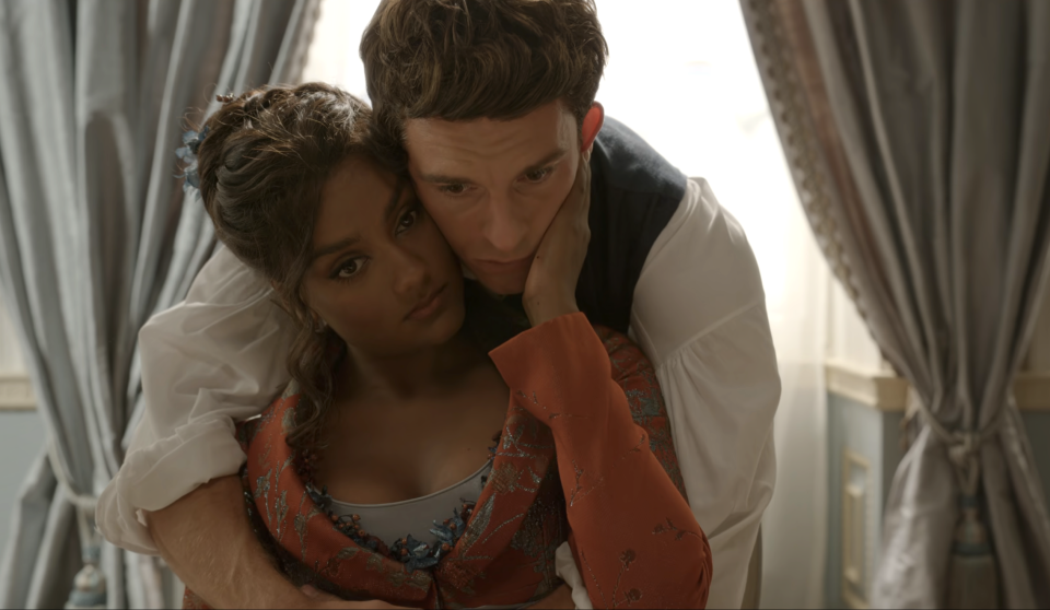Simone Ashley and Jonathan Bailey embrace in a tender moment, set in a luxurious room with draped curtains