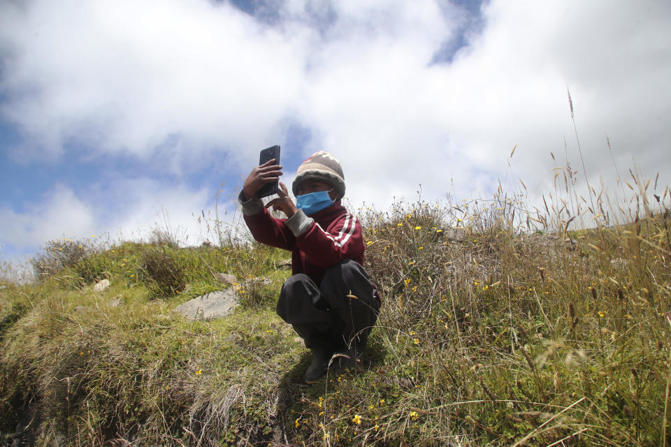 Adan Cholango, con mascarilla para protegerse del coronavirus y sentado en lo alto de una colina, busca una buena cobertura con un celular para obtener las instrucciones para una reunión virtual entre sus padres y su profesor en su primera semana de clases, en Cangahua Alto, Ecuador, el 3 de septiembre de 2020. Cholango es uno de los muchos estudiantes que, debido a la pandemia, empieza el curso con una batalla para obtener una conexión a internet estable en zonas rurales, con deudas para adquirir un dispositivo móvil y con poco conocimiento sobre el uso de las nuevas herramientas académicas. (AP Foto/Dolores Ochoa)